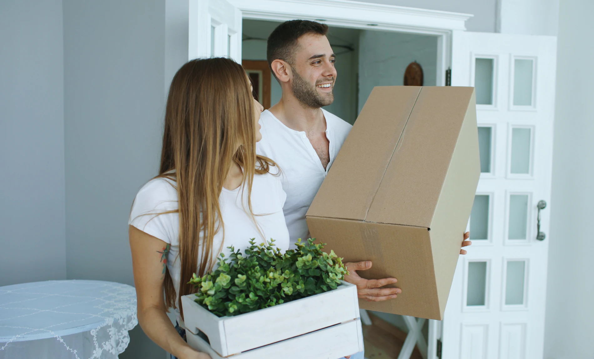 A smiling couple carrying moving boxes into their new home